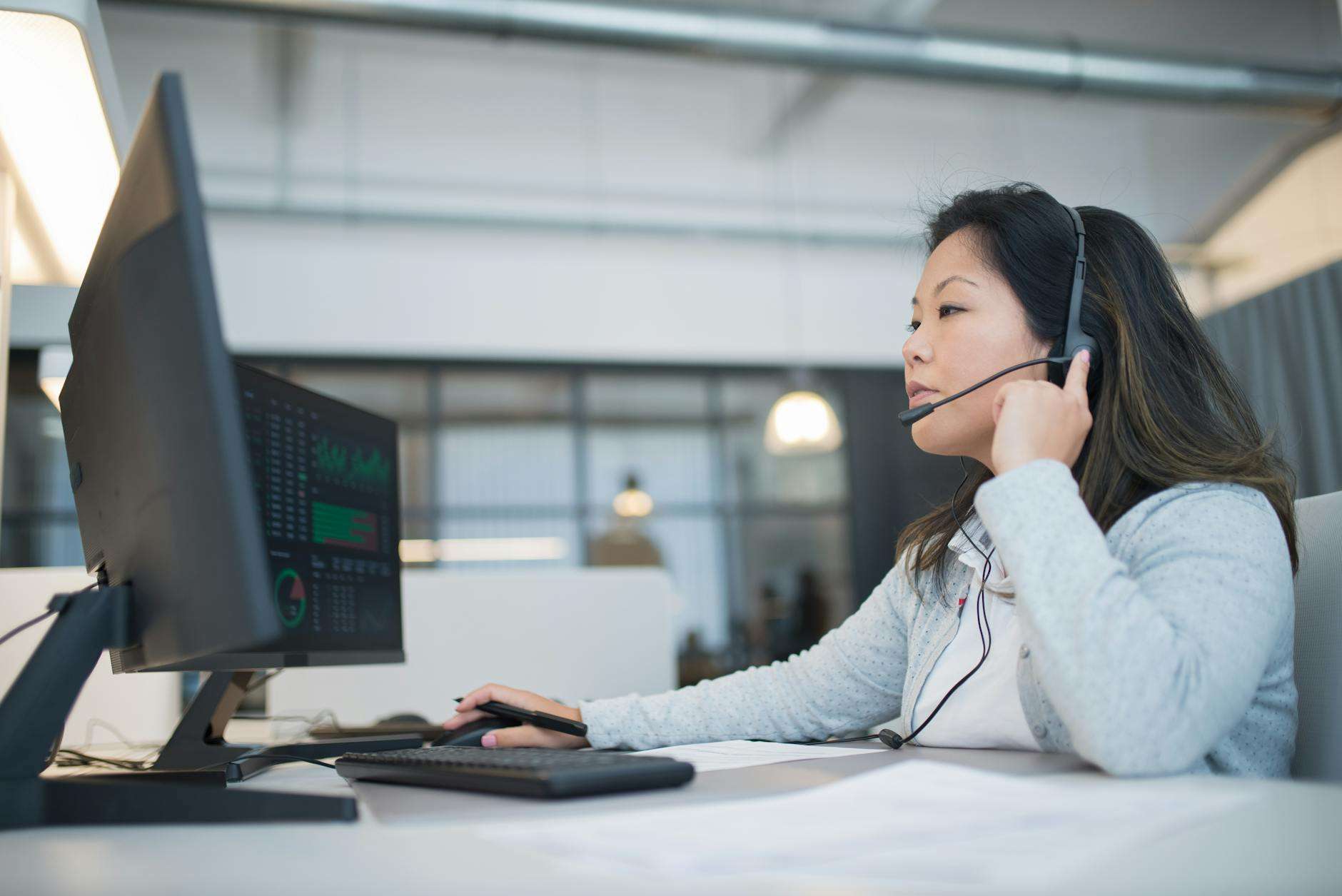 Customer service professional wearing a headset working at a modern office desk with AI-powered tools