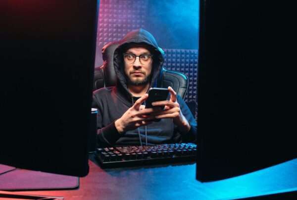 Person in a dark environment using a smartphone surrounded by technology, representing mobile cybersecurity threats