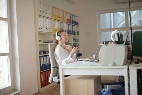 Woman using smartphone and headphones at modern office desk representing professional on-hold experience