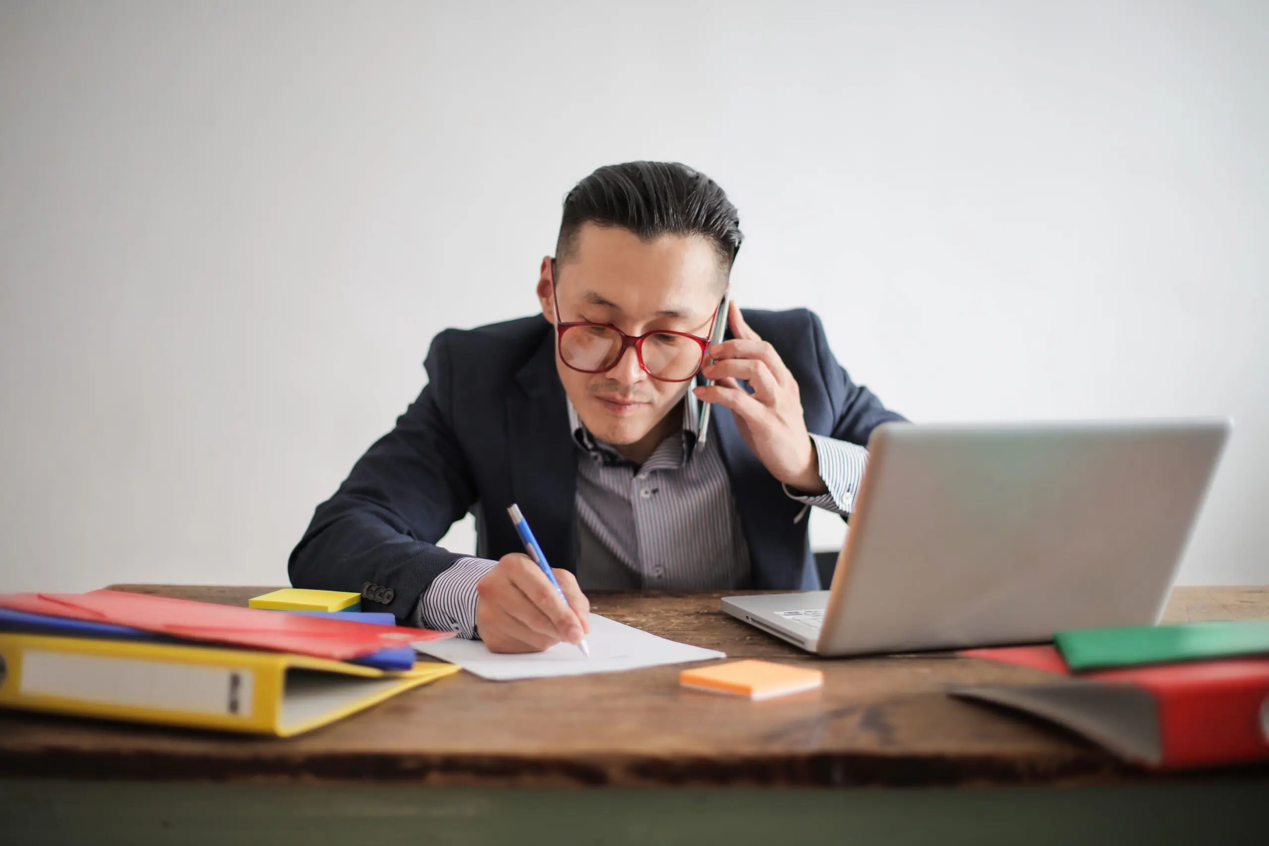 How to Choose a Business Phone System: Key Features That Actually Matter 4 Businessman multitasking with a phone call and laptop at his desk, representing a modern business phone system in daily use