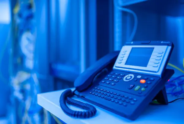 Close-up of a modern office VoIP business phone illuminated with blue lighting, representing reliable digital voice communication