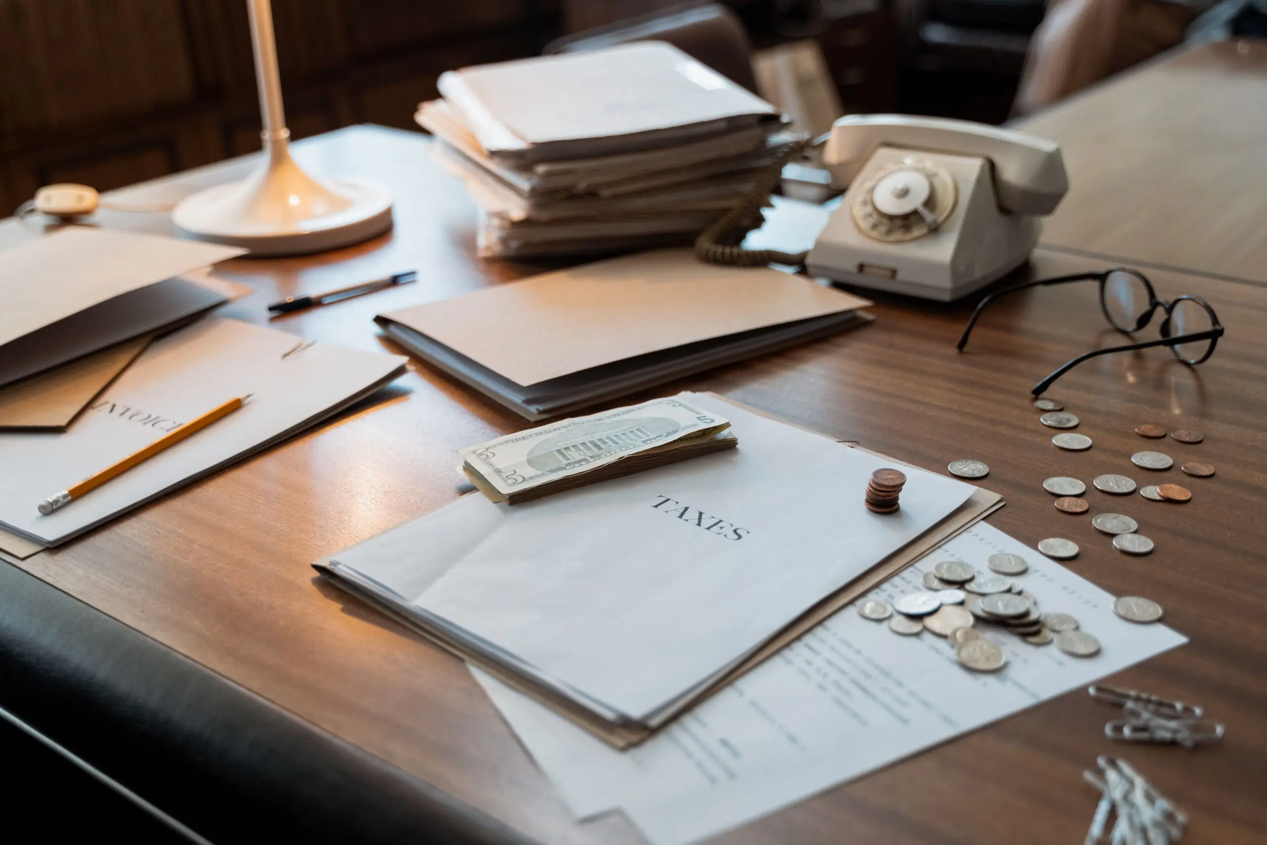 The Real Line-Item Costs of Keeping Your Legacy Phone System: A 2026 Budgeting Guide 3 Old office phone next to tax documents, coins, and a calculator, representing the hidden line-item costs of a legacy phone system