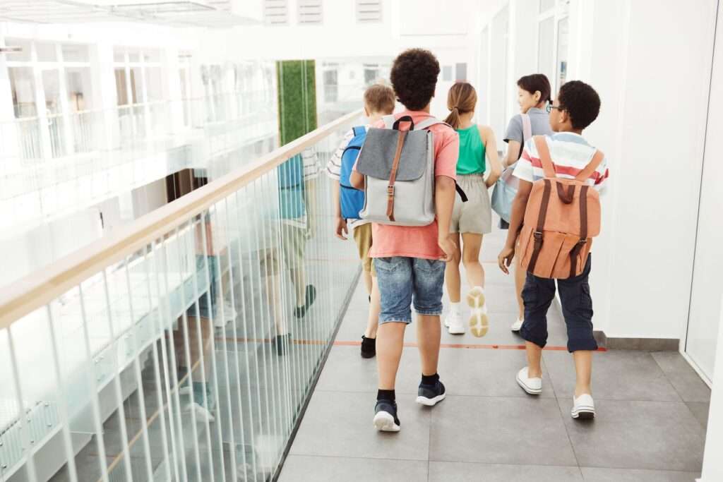 Building a Reliable Emergency Communication Plan for Schools: What District Leaders Should Look For 2 Students walking through a bright, modern school hallway, representing the everyday campus environment emergency communication systems are designed to protect