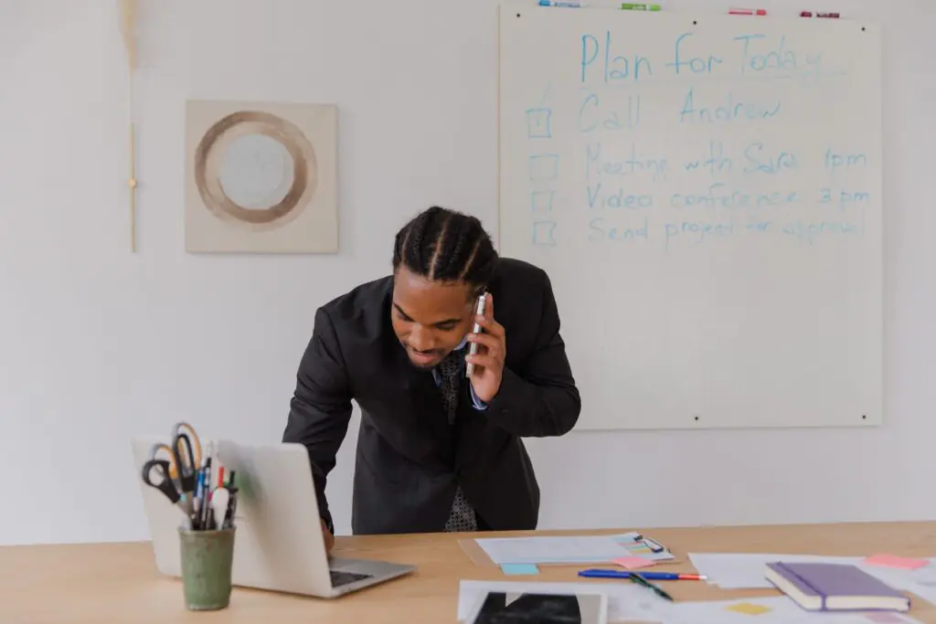 Businessman at an office desk answering a phone call while working on a laptop, representing a small business evaluating an answering service