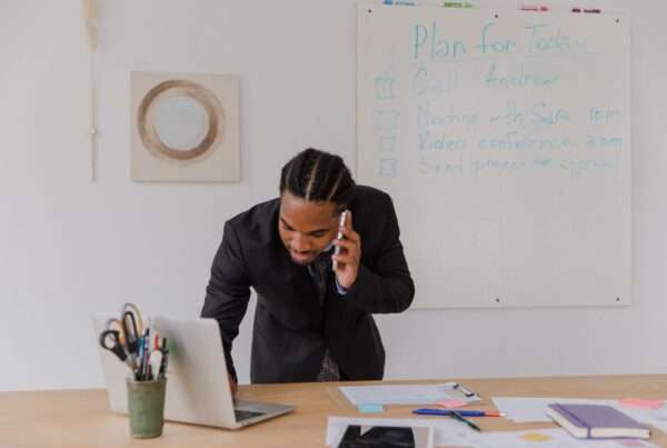 Businessman at an office desk answering a phone call while working on a laptop, representing a small business evaluating an answering service