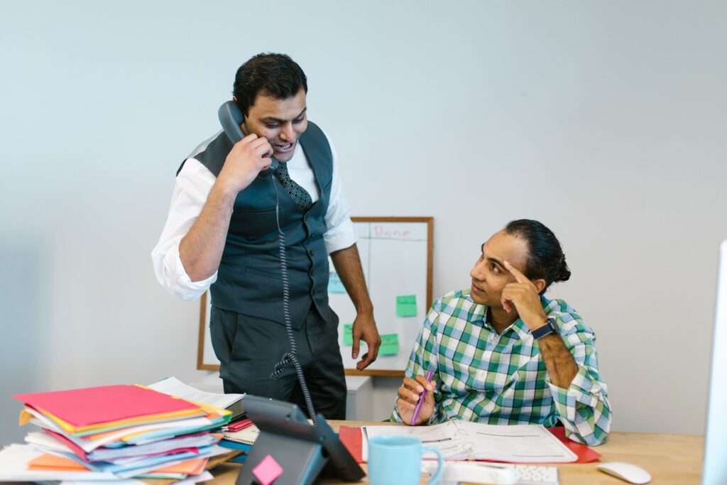 Business professional talking on a business phone number in a modern office, discussing calls with a colleague