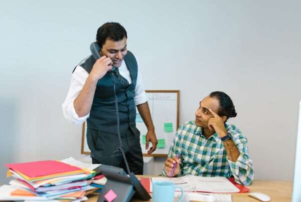 Business professional talking on a business phone number in a modern office, discussing calls with a colleague