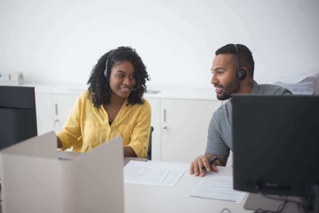 Two customer support agents wearing headsets working together at a modern contact center workstation