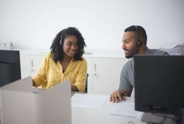 Two customer support agents wearing headsets working together at a modern contact center workstation