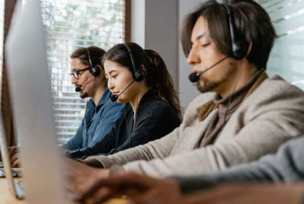 Three contact center agents wearing headsets working at desks in a modern office