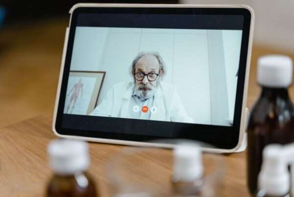 Physician at a desk in a clinic conducting a telehealth video visit on a computer monitor, supported by a reliable business internet connection