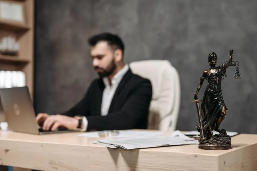 Attorney working on a laptop at a law office desk beside a statue of Lady Justice