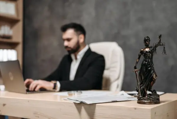 Attorney working on a laptop at a law office desk beside a statue of Lady Justice
