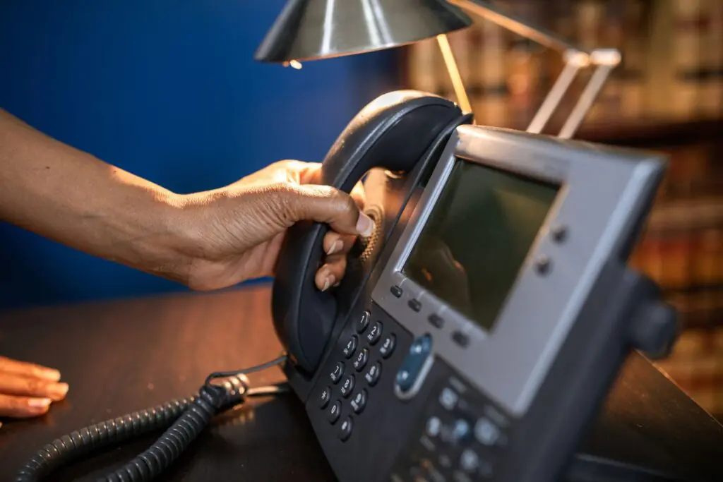 A hand lifting the handset of a black office desk telephone, illustrating a business phone system audit and replacement evaluation