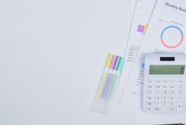 Laptop displaying a budget spreadsheet on a desk beside printed invoices and a calculator during annual technology budget planning