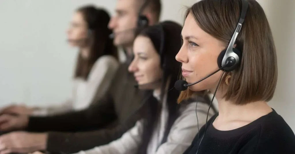 Row of call center agents wearing headsets working at computers