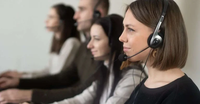 Row of call center agents wearing headsets working at computers