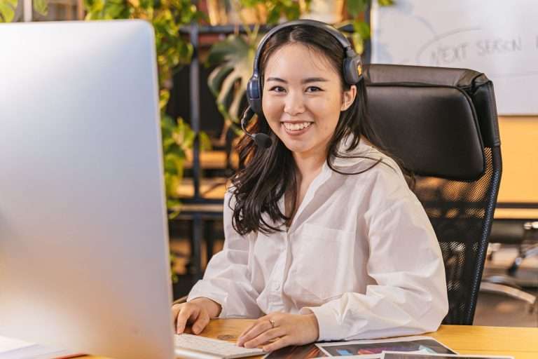 AI Answering Service Adoption Barriers: How to Overcome Them and Roll Out With Confidence 2 Smiling team member wearing a headset sits at a desk with a computer in a bright office, ready to assist callers
