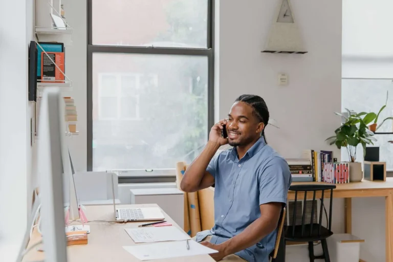 Smiling business owner talking on a mobile phone while seated at a desk in a home office