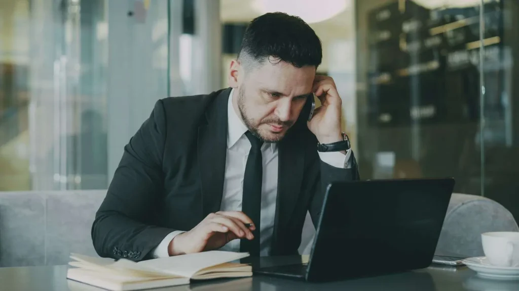Focused business professional in a suit working on a laptop and phone evaluating business communication provider options