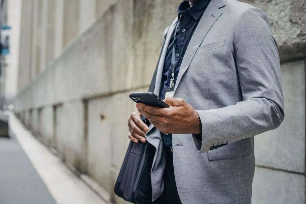 Business professional in a gray suit checking a smartphone while walking past a concrete building