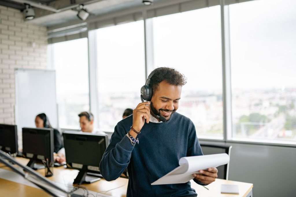 Smiling customer service agent wearing a headset reviews notes while helping a caller in a modern office