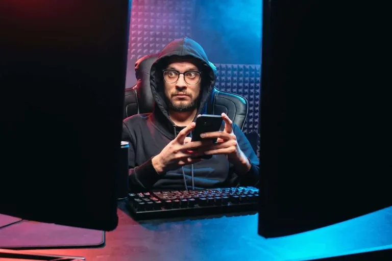 Person in a dark environment using a smartphone surrounded by technology, representing mobile cybersecurity threats