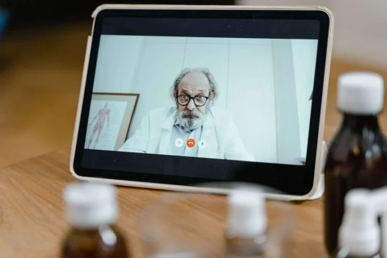 Physician at a desk in a clinic conducting a telehealth video visit on a computer monitor, supported by a reliable business internet connection