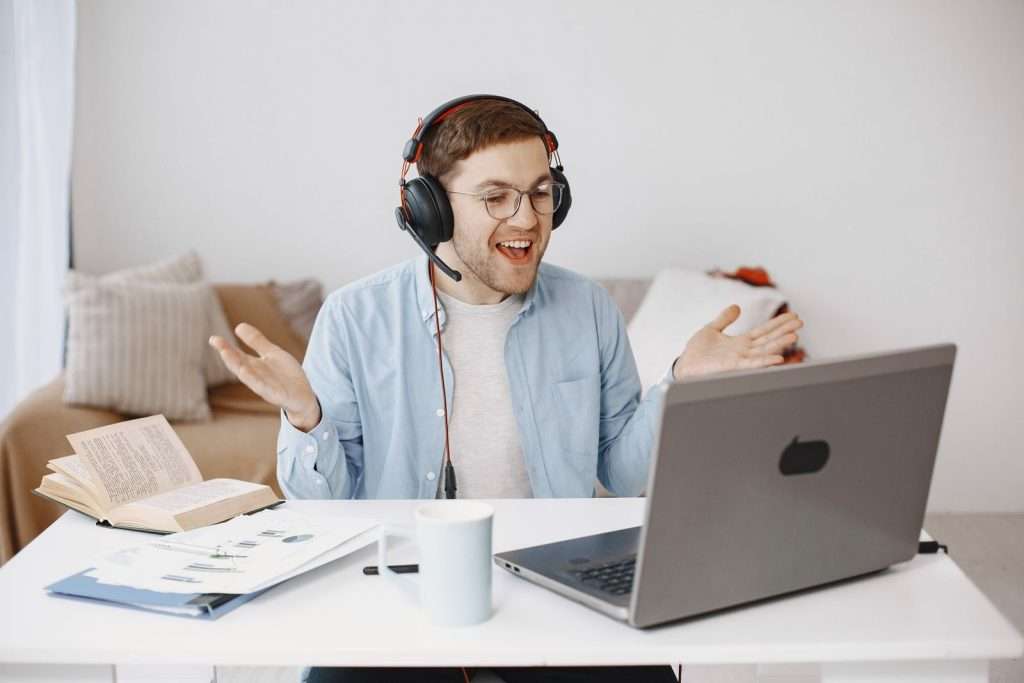 Smiling remote employee wearing a headset talks on a laptop call from a bright home office