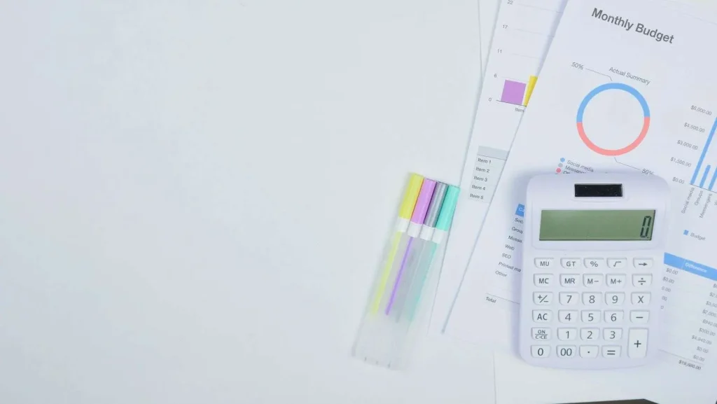 Laptop displaying a budget spreadsheet on a desk beside printed invoices and a calculator during annual technology budget planning