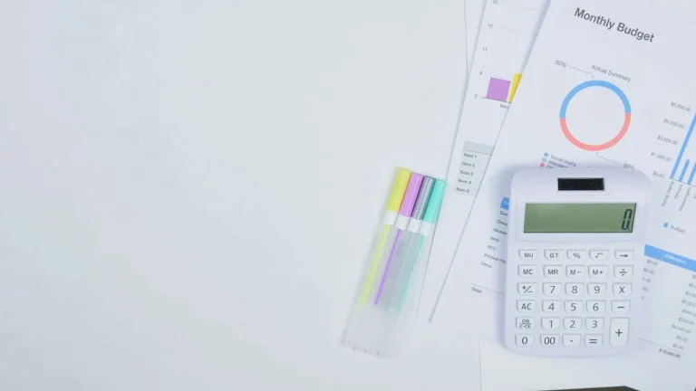 Laptop displaying a budget spreadsheet on a desk beside printed invoices and a calculator during annual technology budget planning