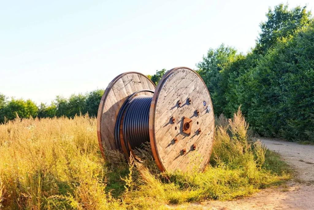 A wooden reel of fiber cable resting in a field beside a rural road, staged for a regional broadband build-out