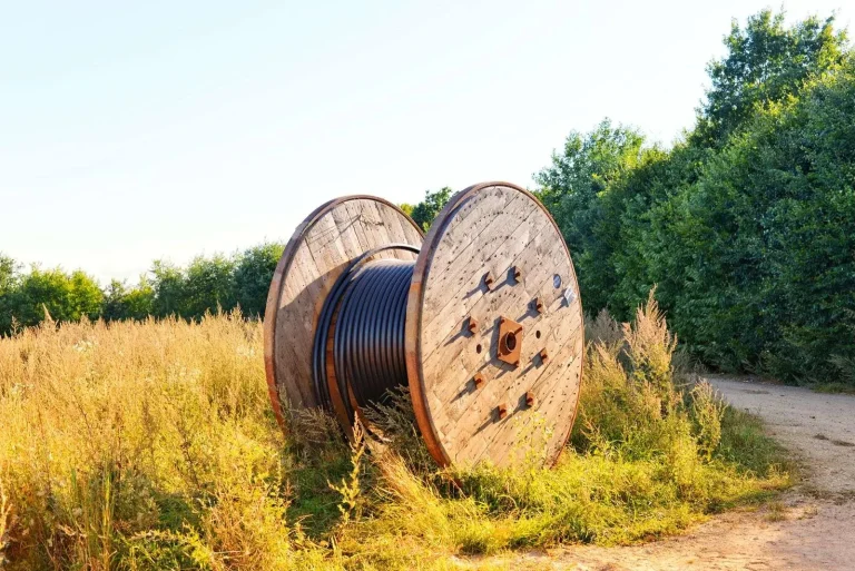A wooden reel of fiber cable resting in a field beside a rural road, staged for a regional broadband build-out
