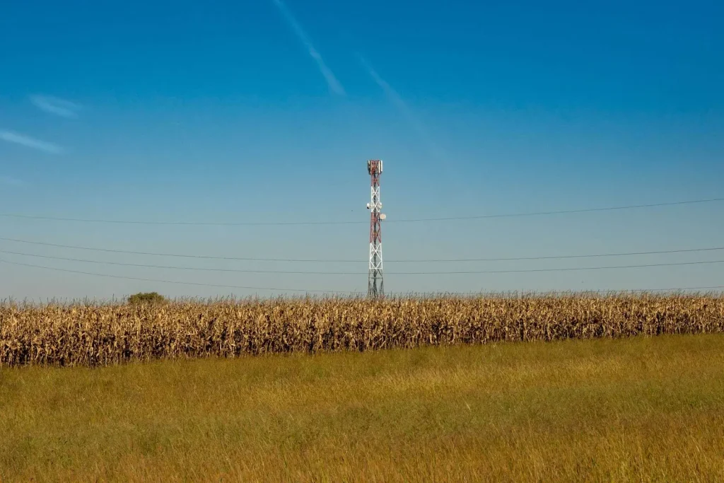 Communication tower standing in a rural field under a clear blue sky, representing expanding broadband connectivity