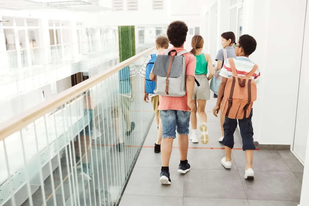 Students walking through a bright, modern school hallway, representing the everyday campus environment emergency communication systems are designed to protect