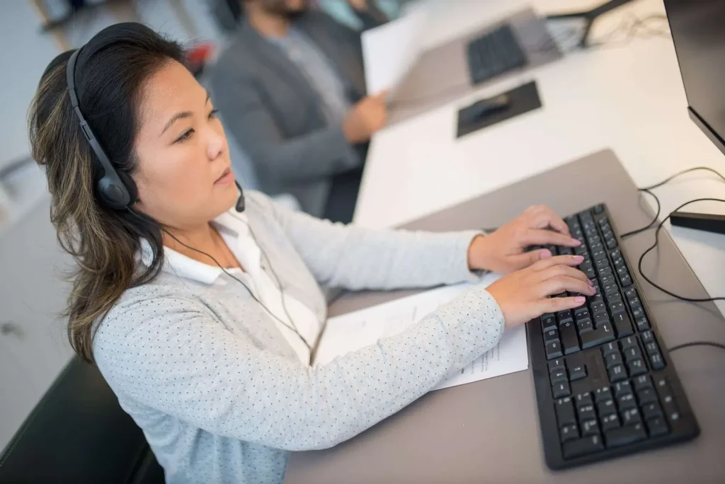 Customer support professional wearing a headset typing on a keyboard at an office workstation