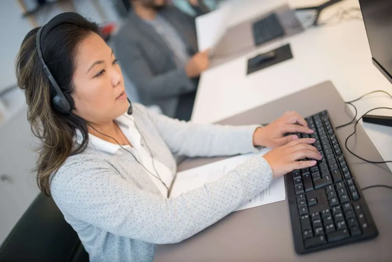 Customer support professional wearing a headset typing on a keyboard at an office workstation