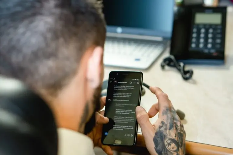 Business professional using a smartphone at a desk with a laptop, representing SMS API pricing and business text messaging