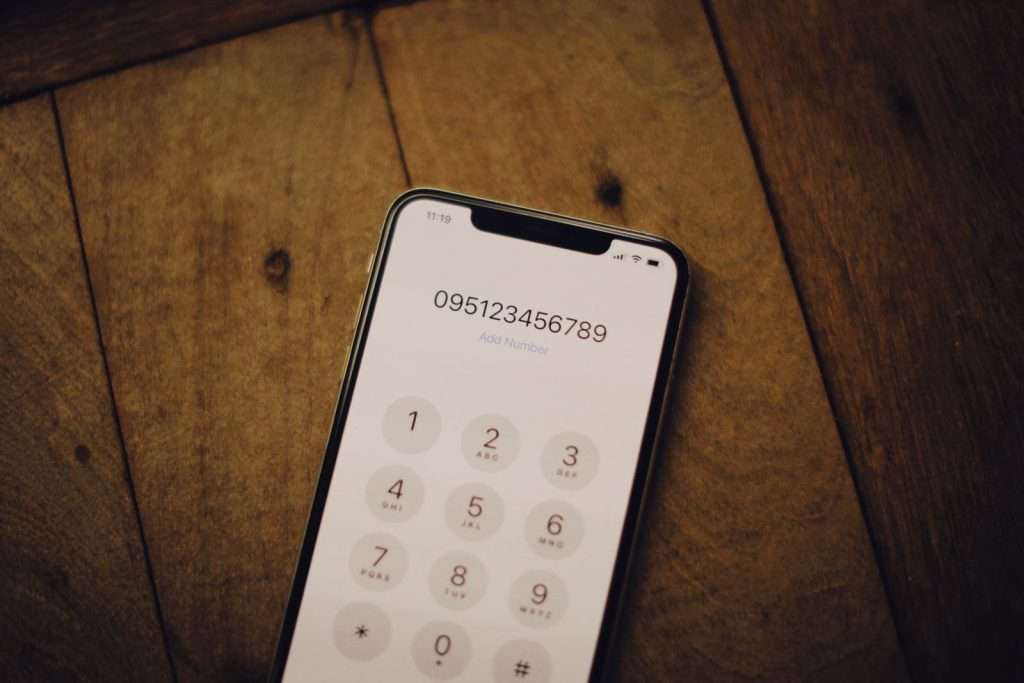 Smartphone dial pad on a wooden desk showing the letters assigned to each number key, illustrating how vanity phone numbers spell words
