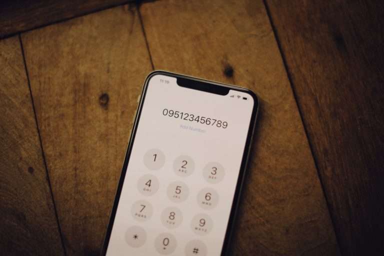 Smartphone dial pad on a wooden desk showing the letters assigned to each number key, illustrating how vanity phone numbers spell words